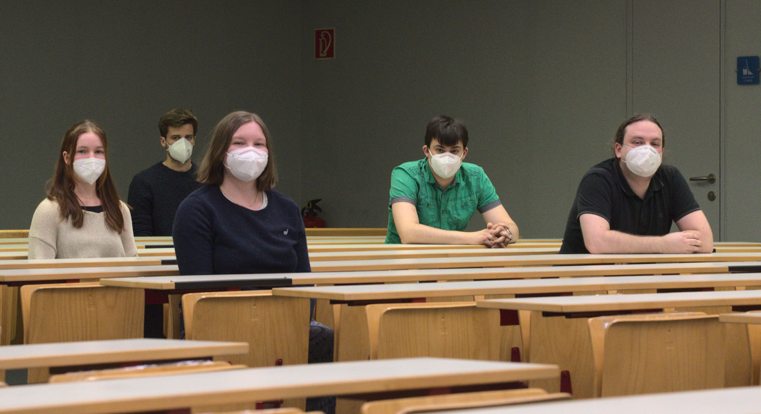 Gruppenfoto der Kandidat_innen: 5 Studierende, die FFP2-Masken tragen, sitzen in einem Hörsaal